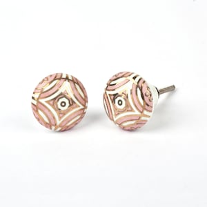 Peut inclure: Deux boutons de meuble décoratifs. Les boutons sont ronds avec un motif géométrique rose, blanc et doré. Les boutons ont une vis métallique pour la fixation. Les boutons sont sur fond blanc.