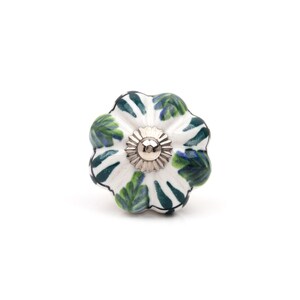 May include: A round, flower-shaped ceramic cabinet knob featuring a white base with hand-painted green and blue leaf patterns. The center of the knob has a silver-toned metal hardware piece with a scalloped edge and a central screw hole.