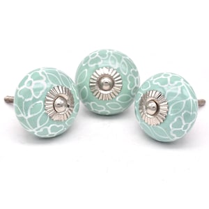 May include: Three ceramic cabinet knobs with a light green background and white floral pattern. The knobs have a silver metal base.