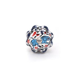May include: A decorative ceramic cabinet knob with a floral and animal design. The knob features a white base with blue and red floral patterns and two blue tiger illustrations. The knob has a silver metal center.
