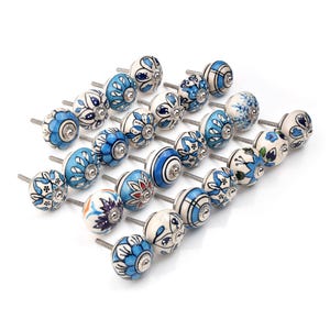 Assorted hand-painted ceramic knobs in blue, black and white with mandala and floral motifs for cupboard handles and kitchen decor.