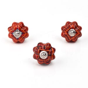 Red ceramic knobs with hand-painted white floral and mandala designs; assorted cabinet knobs for furniture and home décor.