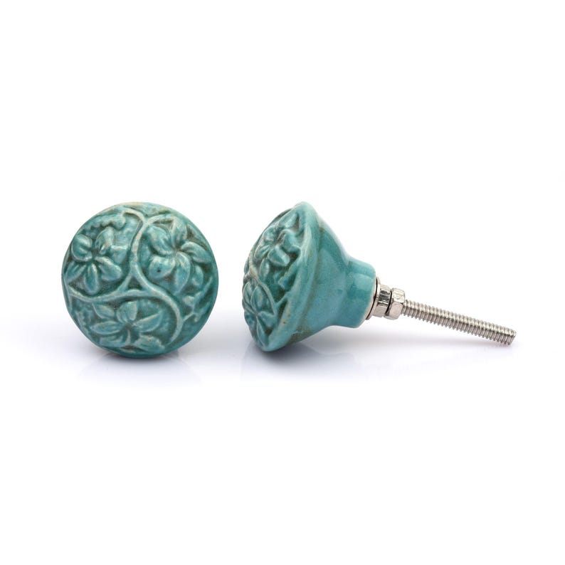 May include: A collection of twelve decorative cabinet knobs in various colours and patterns. Each knob features a round or oval shape with a metal bolt extending from the back. The designs include floral, geometric, and solid textures in shades of green, blue, orange, purple, white, and grey.