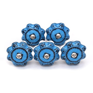 May include: Five blue ceramic cabinet knobs with a starburst design and silver-colored hardware. The knobs have a black geometric pattern around the center and edges. The knobs are arranged on a white background.
