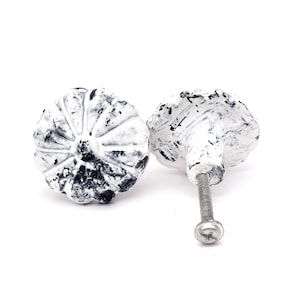 May include: Two white and black cabinet knobs with a textured finish. The knobs are shaped like pumpkins, with black speckles. One knob is upright, the other on its side. Each has a silver screw for attaching to furniture.