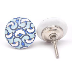 Op de afbeelding: Twee keramische kastknoppen. Eén knop heeft een lichtblauwe achtergrond met een wit en blauw bloemmotief. De andere knop is wit met een zilverkleurige metalen basis en schroef.