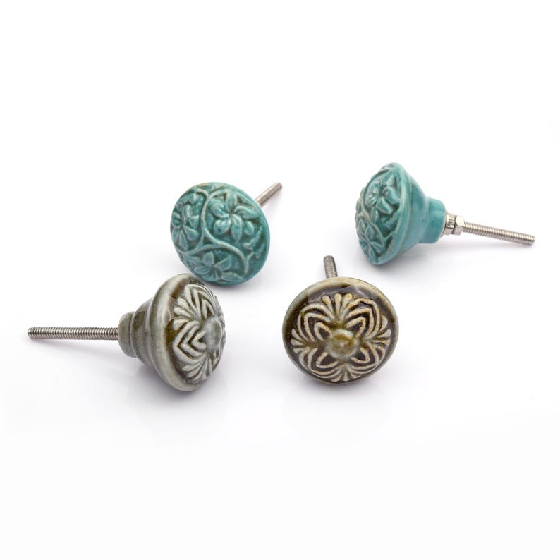 May include: A collection of twelve decorative cabinet knobs in various colours and patterns. Each knob features a round or oval shape with a metal bolt extending from the back. The designs include floral, geometric, and solid textures in shades of green, blue, orange, purple, white, and grey.