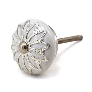 White ceramic cabinet knob with a silver flower motif and gold center; decorative furniture knob for cabinets and drawers.