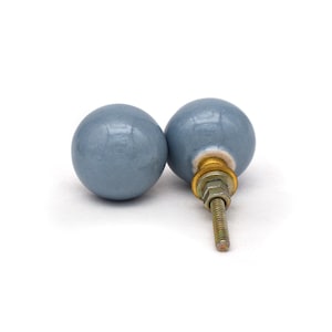 May include: Two pale blue ceramic cabinet knobs with a spherical design. Each knob features a metal screw and hardware for fitting. The knobs are set against a white backdrop.