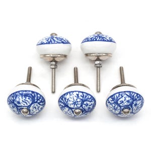 Pode incluir: Cinco puxadores de arm&aacute;rio de cer&acirc;mica branca com padr&otilde;es florais azuis. Os puxadores t&ecirc;m formato arredondado com base e parafuso de metal prateado. O design apresenta um padr&atilde;o azul em forma de &aacute;rvore sobre fundo branco.