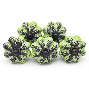 May include: Four green ceramic cabinet knobs with black splatter paint and a black metal center. The knobs are shaped like a flower with five petals.