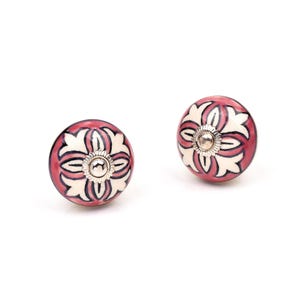 May include: Two round ceramic cabinet knobs featuring a deep pink and cream-colored floral pattern. Each knob has a central silver-toned metal hardware piece with a scalloped edge, providing a decorative accent to the smooth, rounded surface.