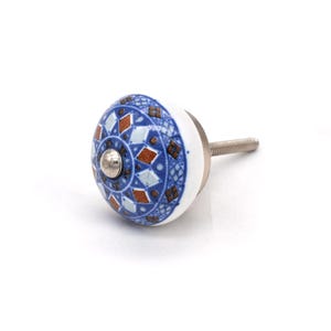 May include: A decorative ceramic cabinet knob with a white base and a patterned design in blue, rust, and white. The knob has a silver metal screw for attachment. The design features diamond and circular patterns.