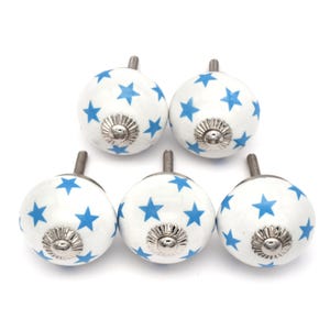 Könnte beinhalten: Satz mit sechs weißen Keramik-Schrankknöpfen mit blauem Sternenmuster. Jeder Knopf hat eine silberne Metallbasis.