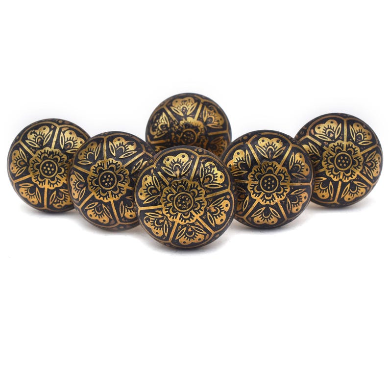 Etched brass flower cabinet knob with ornate gold pattern on dark background; decorative cabinet knobs for dresser hardware.