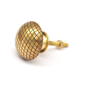 Puede incluir: Un pomo de armario dorado con un patrón geométrico. El pomo tiene una forma redonda y un vástago roscado.