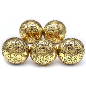 Op de afbeelding: Vijf ronde gouden ornamenten met een gegraveerd bloemenpatroon op het oppervlak.