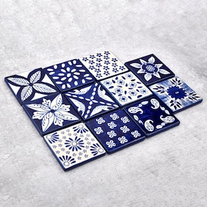 May include: A collection of twelve square ceramic coasters with intricate blue and white floral and geometric patterns. The coasters are arranged on a gray surface, showcasing a variety of designs including flowers, leaves, and abstract shapes.