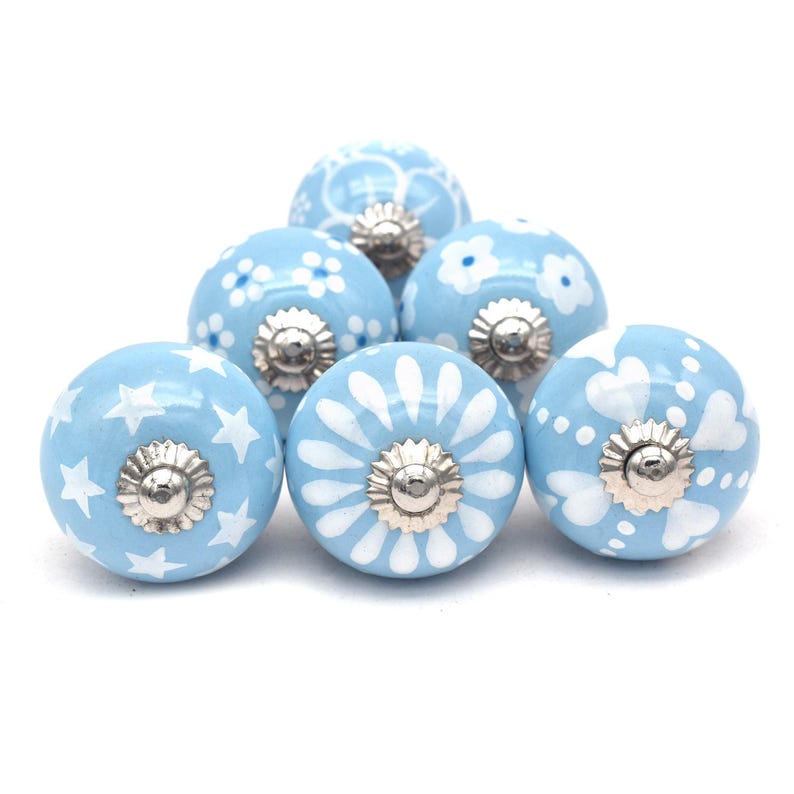 Hand-painted sky-blue ceramic knobs with assorted white designs (stars, flowers, stripes) for cabinets and drawers.