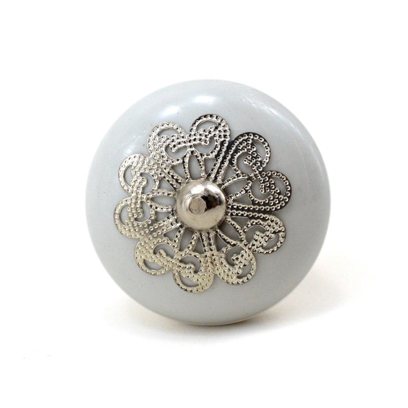 White ceramic cabinet knob with a silver flower motif and gold center; decorative furniture knob for cabinets and drawers.