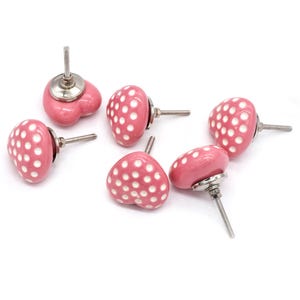 May include: Six pink ceramic heart-shaped cabinet knobs with white polka dots and silver screw posts.