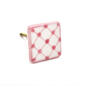 Può includere: Pomello quadrato in ceramica con sfondo bianco e motivo a griglia rosa con pois. I bordi sono anch'essi rosa. Il pomello ha una vite in ottone per l'installazione.