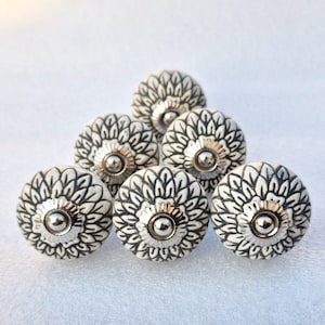 Op de afbeelding: Set van zes witte keramische kastknoppen met een zwart bloemenmotief en zilveren accenten.