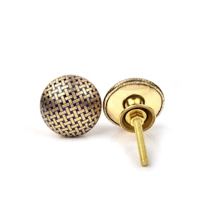 Può includere: Due pomelli decorativi per mobili. I pomelli sono rotondi con una base in metallo color oro e un motivo intrecciato blu e oro sul davanti. Un pomello è mostrato con la vite e la piastra posteriore visibili. L'altro pomello è mostrato frontalmente.