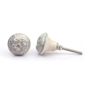 May include: A collection of twelve decorative cabinet knobs in various colours and patterns. Each knob features a round or oval shape with a metal bolt extending from the back. The designs include floral, geometric, and solid textures in shades of green, blue, orange, purple, white, and grey.