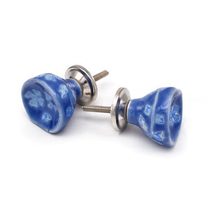 Puede incluir: Dos pomos de armario de cerámica azul con base y tornillo de metal plateado. Los pomos tienen un diseño floral blanco.