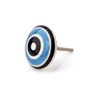 May include: A ceramic cabinet knob with a circular design. The knob features concentric rings of black, light blue, and white. The knob has a silver screw for attachment. The knob is a decorative element for furniture.