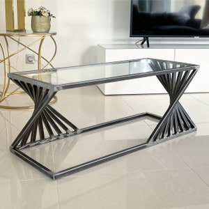 Peut inclure: Une table basse moderne avec un plateau en verre et un piétement métallique géométrique unique. Le piétement est en métal noir et a une forme torsadée en sablier.