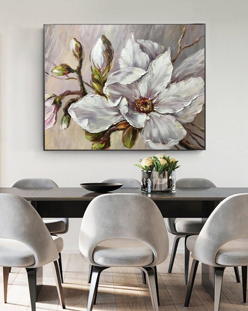 May include: A painting of a white magnolia flower with green leaves and buds. The flower is in focus and the background is blurred.