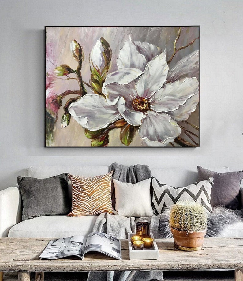 May include: A painting of a white magnolia flower with green leaves and buds. The painting is done in a realistic style with thick brushstrokes. The background is a soft pink and purple.