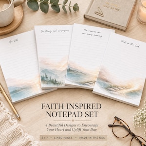 May include: A Faith Inspired Notepad Set with four lined notepads, each featuring a different inspirational quote and a watercolor landscape design. The notepads are 5 x 7 inches and made in the USA. A gold pen and glasses are also visible.