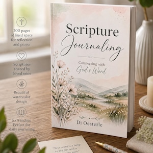 May include: A white book titled Scripture Journaling: Connecting with God's Word by Di Oesterle, featuring a watercolor landscape of hills and flowers. The cover lists 200 pages, 6 x 9 inches, and scripture sharing. A card with Psalm 119:105 and a floral pen are nearby.