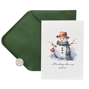 May include: Watercolor Christmas card featuring a snowman with a brown hat, scarf, and mittens. The card includes the text "...and He makes you white as snow. Isaiah 1:18." An olive green envelope and a "Merry Christmas" sticker are also visible.