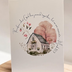 May include: A white greeting card featuring a watercolor illustration of a quaint house with a black roof, surrounded by pink flowers and a tree. The card has the text "Therefore what God has joined together, let no one separate - Mark 10:9."