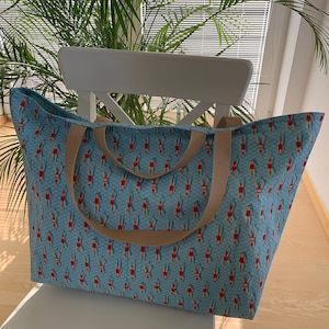 May include: A large blue tote bag with tan straps. The bag is printed with a repeating pattern of women in red swimsuits swimming in a blue pool.