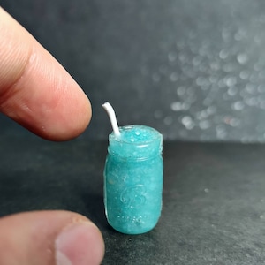 May include: A miniature glass jar filled with a blue slushie and a white straw. The jar has a clear glass lid and a white label with a number on it.