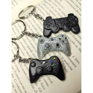 Può includere: Tre portachiavi argentati e neri a forma di controller per videogiochi. I portachiavi sono attaccati a anelli portachiavi argentati.