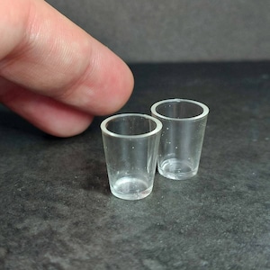May include: Two clear glass shot glasses on a grey surface.
