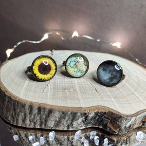 Può includere: Tre anelli regolabili con diversi design. Il primo anello presenta un girasole giallo, il secondo anello ha una mappa del mondo vintage e il terzo anello ha un'immagine della luna in bianco e nero.
