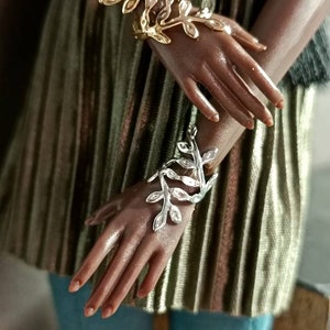 May include: Two gold and silver leaf-shaped bracelets on a person's wrists. The bracelets are made of metal and have a delicate design.
