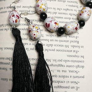 May include: A pair of black tassel earrings with white, red, and yellow oval-shaped beads. The beads have a splatter paint design.