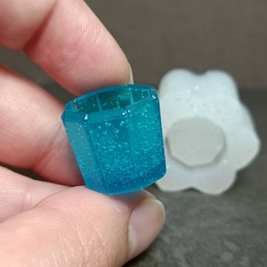 Puede incluir: Un molde de resina azul transparente con forma geométrica y superficie texturizada. El molde está hecho de silicona y está diseñado para fundir resina.