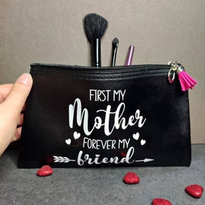 May include: Black zippered makeup bag with a white design that says "First my Mother Forever my friend" with an arrow pointing to the right. There are small white hearts around the text. The bag has a pink tassel zipper pull.