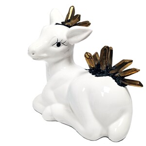 May include: White ceramic deer figurine with gold crystal accents on its head and back. The deer is sitting with its head turned to the side.
