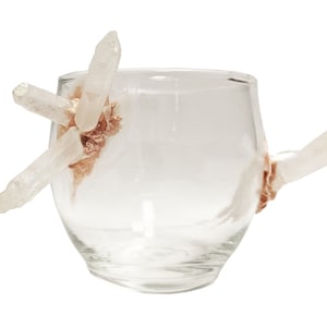 Könnte beinhalten: Eine klare Glas Tasse mit einem einzigartigen Design, das mehrere klare Quarzkristalle aufweist, die an den Seiten befestigt sind. Die Kristalle sind mit goldener Farbe akzentuiert.