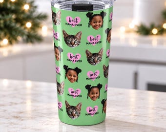 May include: A light green tumbler with a clear lid featuring a repeating pattern of a child's face, a tabby cat's face, and pink hearts containing the black text "best MAMA EVER". The design is printed across the entire exterior of the cup.